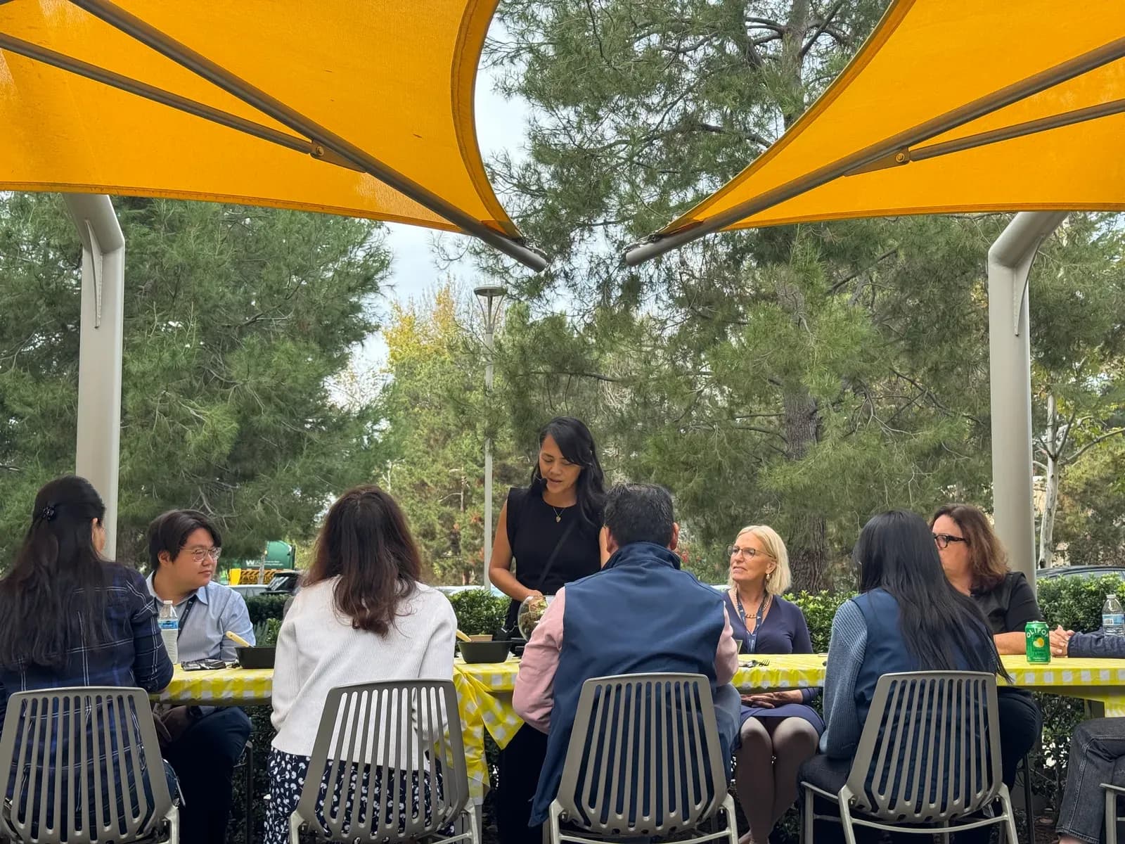 Guests seated along an outdoor workshop table under yellow shade sails