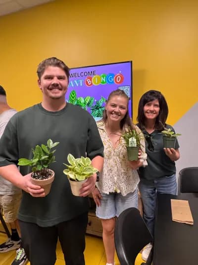 Three Plant Bingo players holding the potted plants they won, the welcome screen behind them