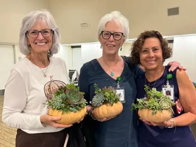 Three guests at a community workshop holding the succulent pumpkins they planted