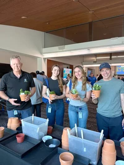 Coworkers holding up their freshly potted plants at a workshop table in their office