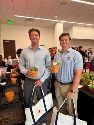 Two coworkers with tote bags holding the plants they potted at an office workshop