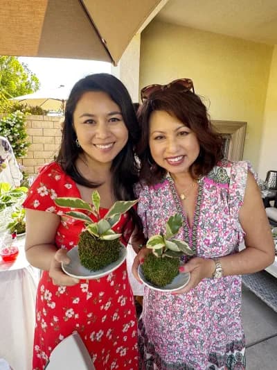 Two friends in summer dresses holding up the kokedama they made