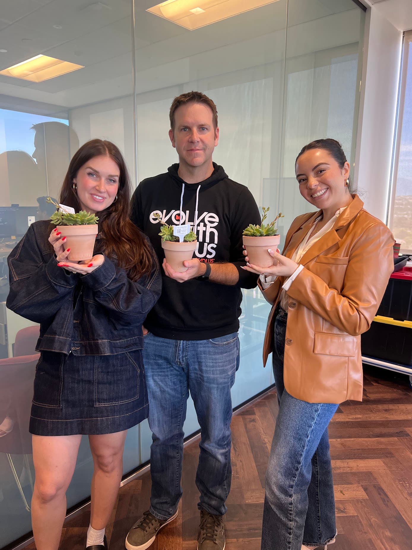 Three coworkers in an office holding small terracotta pots of succulents