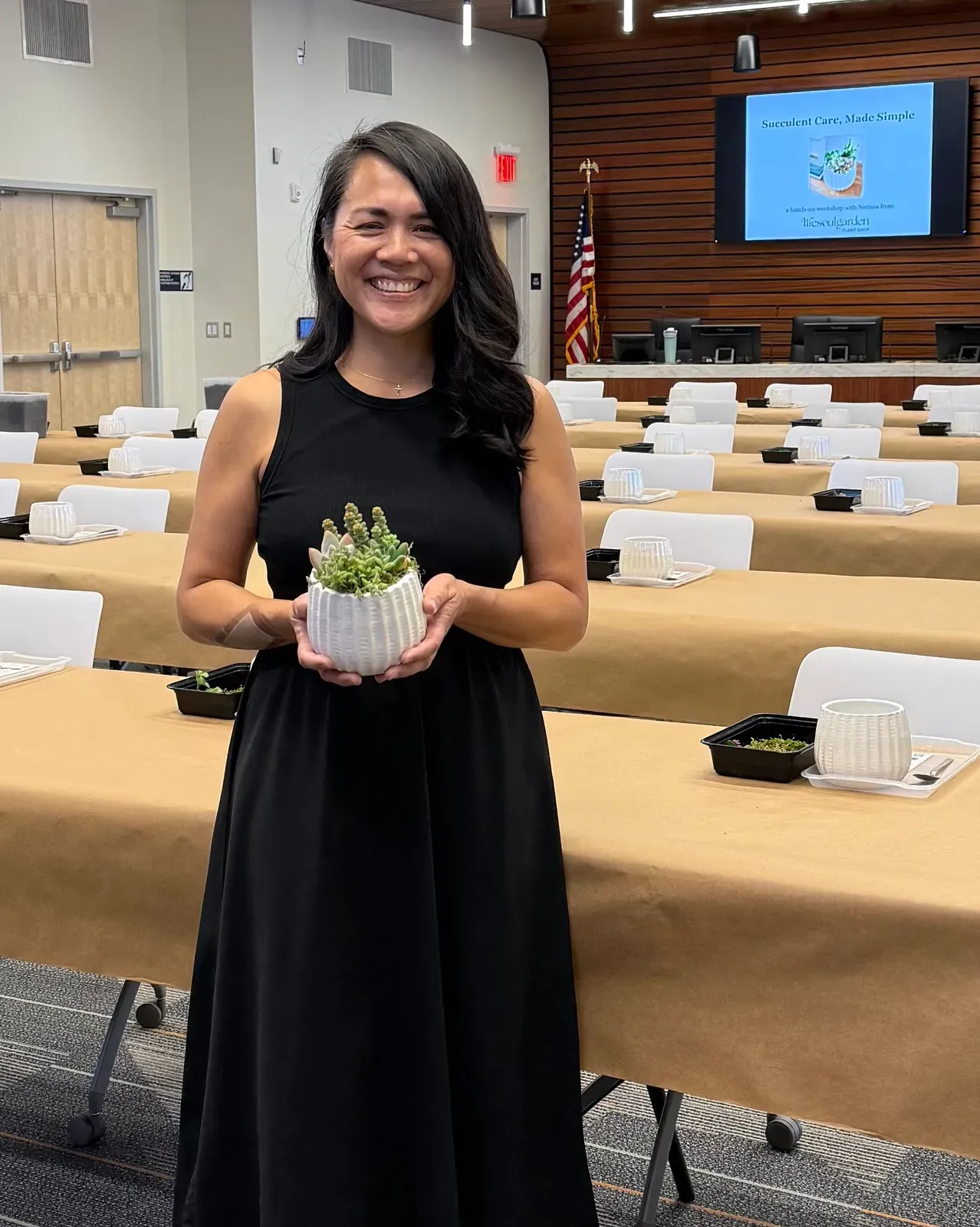 Nerissa holding a succulent bowl in a conference room she has set for a succulent care workshop, a pot waiting at every seat