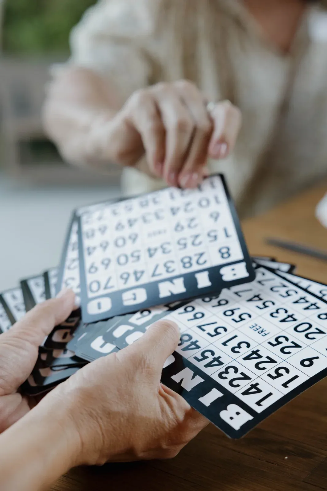 A player fanning out black-and-white BINGO cards above a wooden table